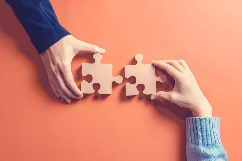 Two hands joining puzzle pieces
