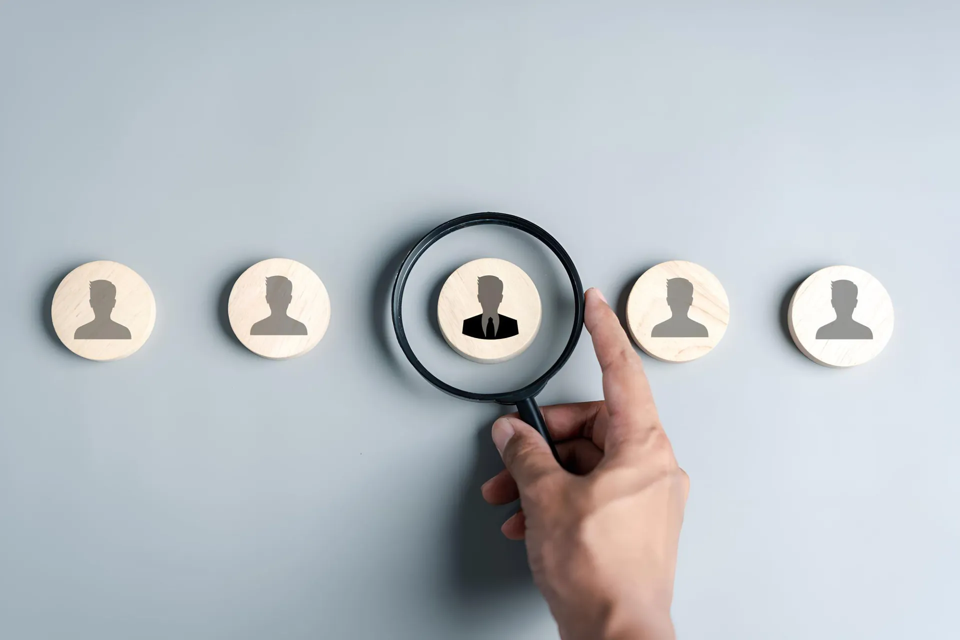 Hand holding a magnifying glass over a row of candidate icons