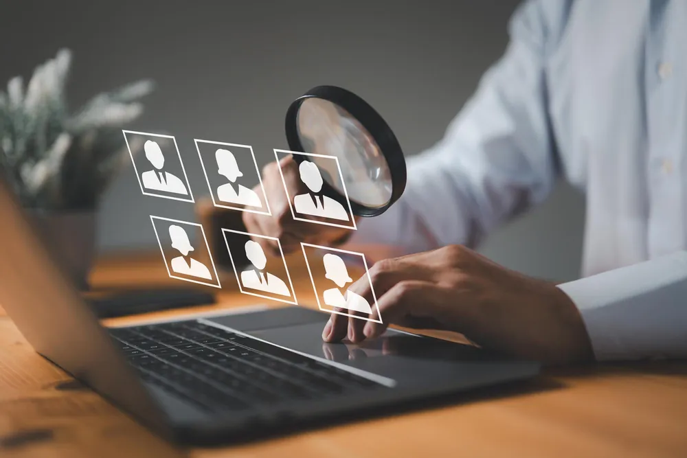 Recruiter reviewing candidate profiles on a laptop with a magnifying glass